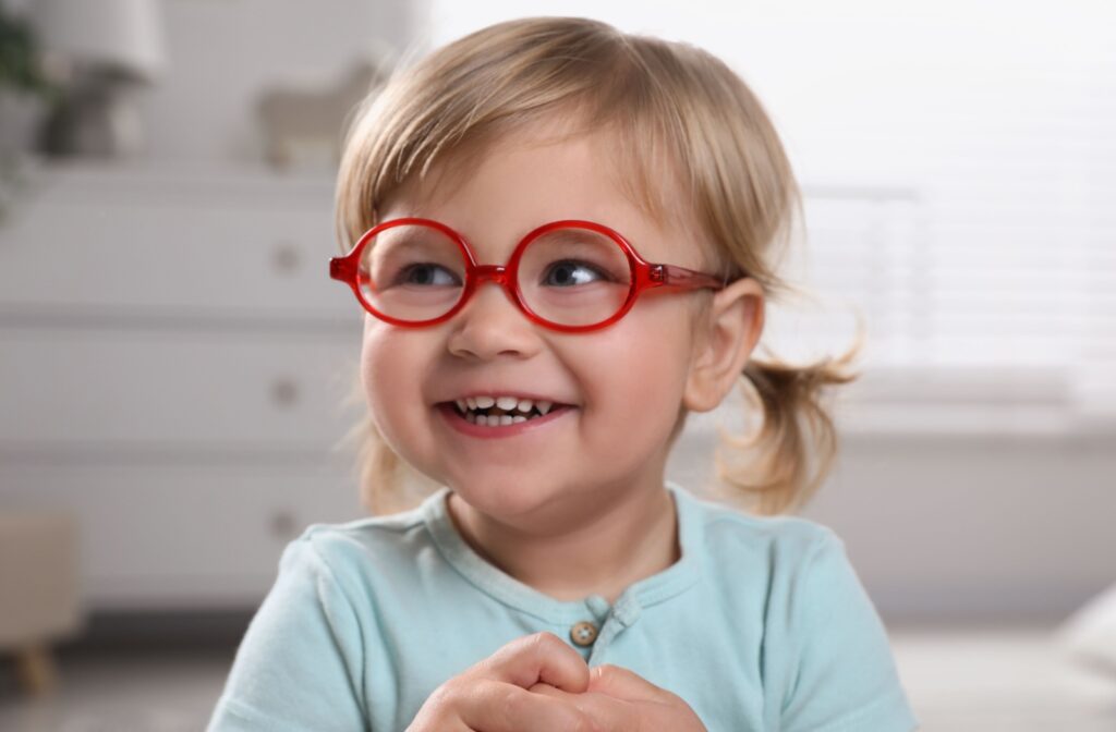 A young child smiles while wearing their bright red glasses.